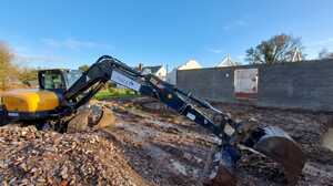 Sibley Contractors excavator digging muddy footings beside a blockwork barn wall in Ashill, Somerset