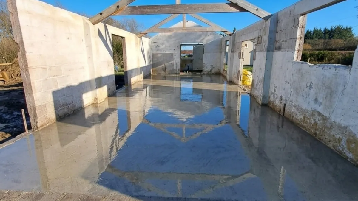 Freshly poured concrete raft foundation inside a barn conversion, reflecting the roof trusses in Ashill, Somerset