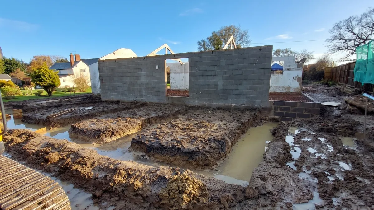 Waterlogged foundation trenches dug in front of barn walls during wet weather in Ashill, Somerset